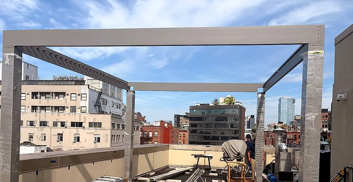 Custom pergola frame being installed on a Manhattan rooftop with city skyline